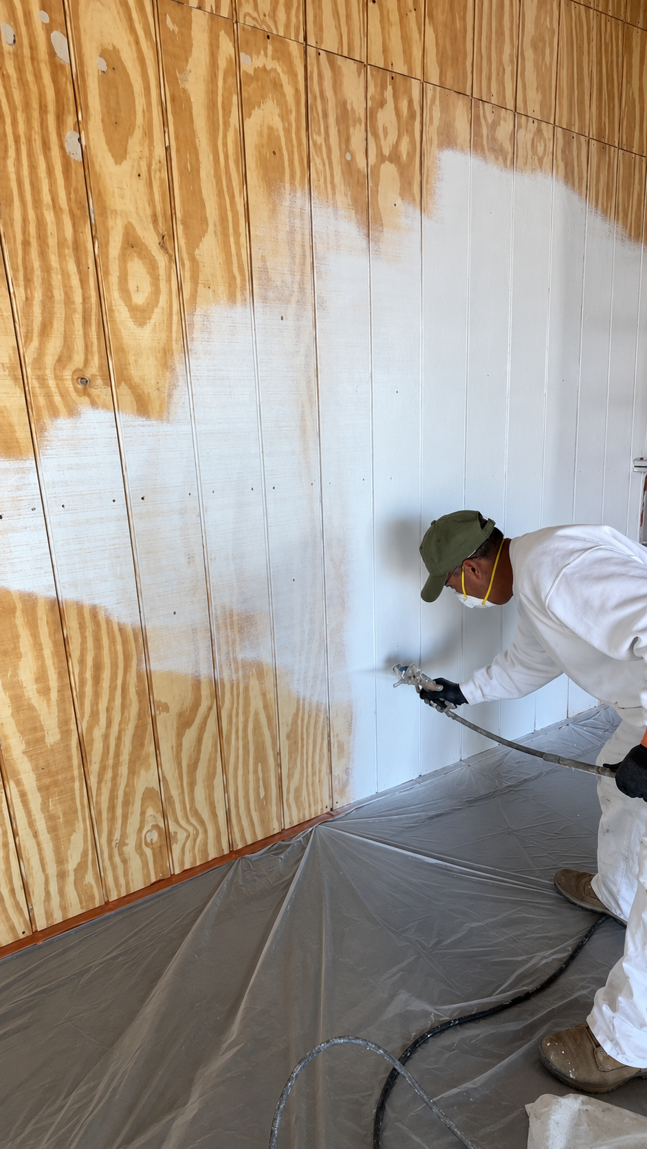 Painter spray painting white primer onto wood paneling during a residential project