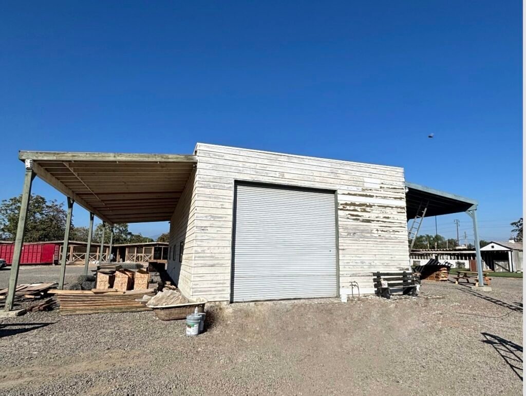 Weathered commercial building exterior before painting, with peeling white siding and a roll-up garage door